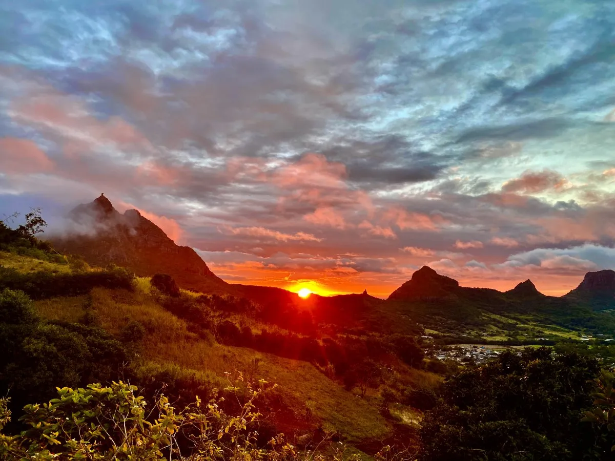 Sunset with reddish hues behind mountains at Terre Rouge-Verdun road in Mauritius under cloudy sky