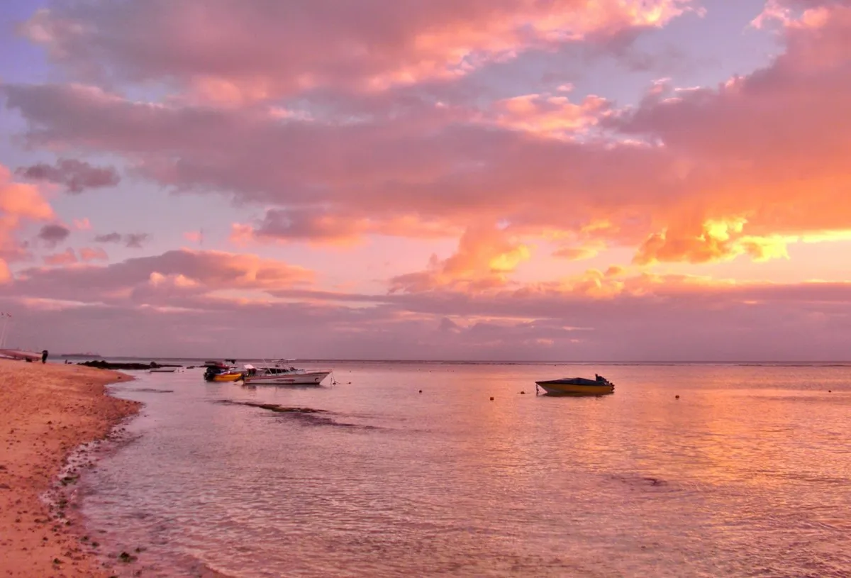 Pink sunset sky over Balaclava beach with fishing boats in the lagoon, Mauritius