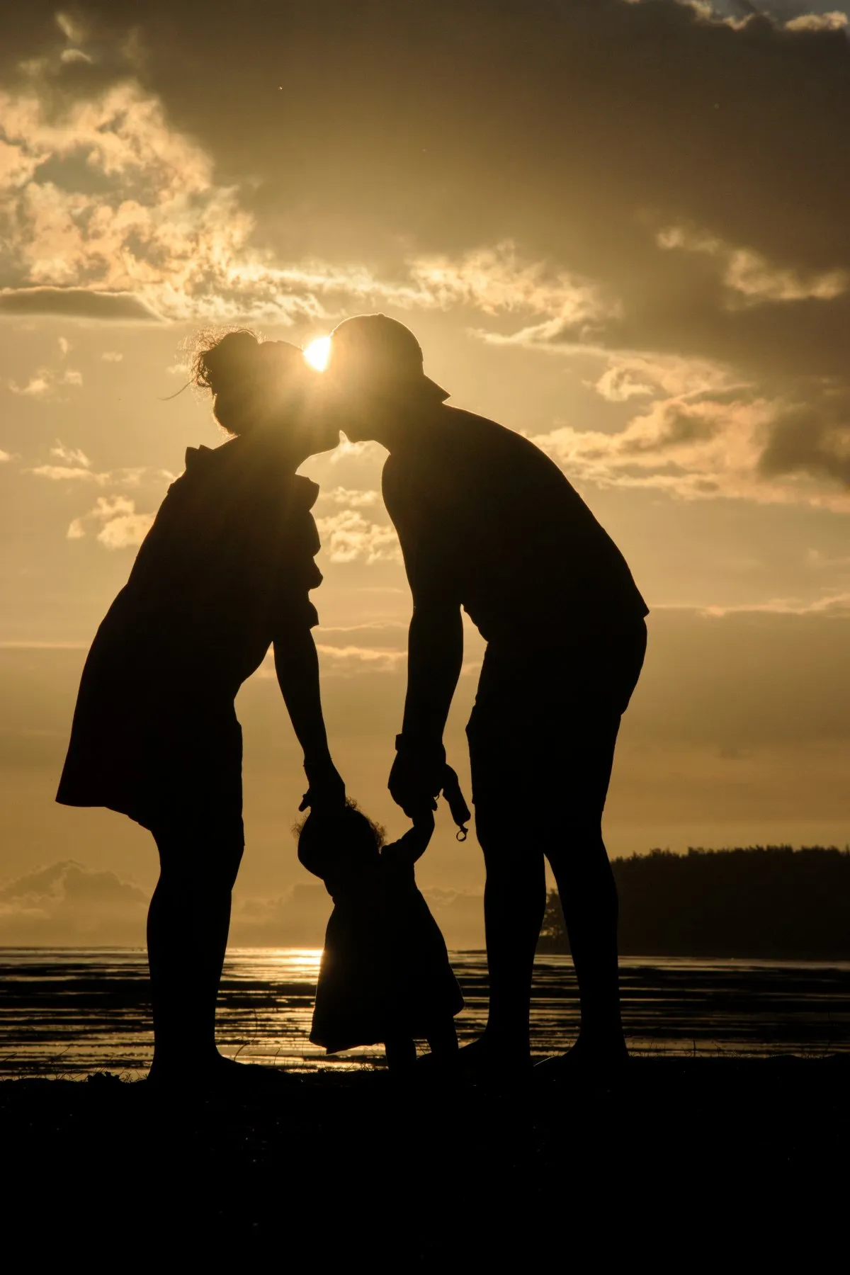 Silhouette of a couple kissing and holding toddler's hand at a beach sunset in Mauritius