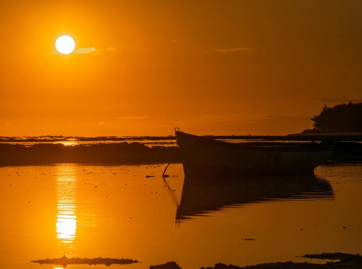 Silhouette of a lonely fishing boat at sunset with calm sea reflections in Mauritius