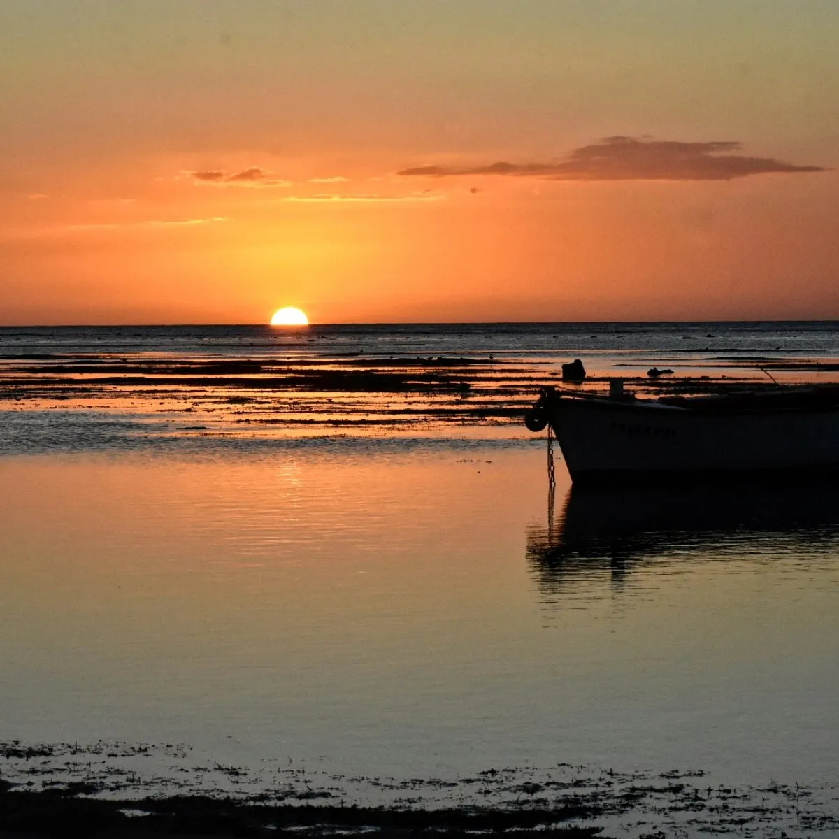 Sun setting behind the horizon over Albion beach with a boat in Mauritius