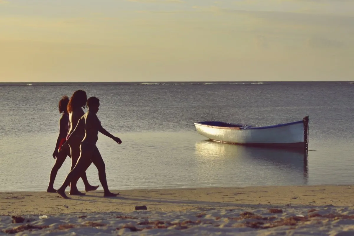 Three Mauritian women walking near a boat along Albion beach in Mauritius