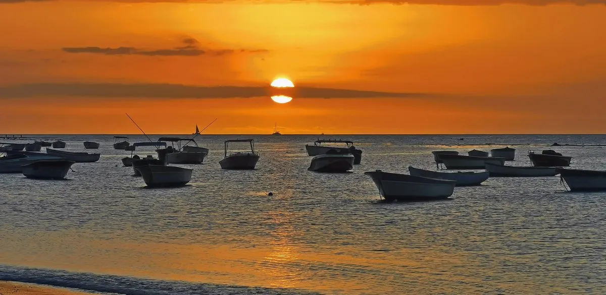 Sunset with boats on the calm lagoon of Tamarin Bay in Mauritius under a partly cloudy sky