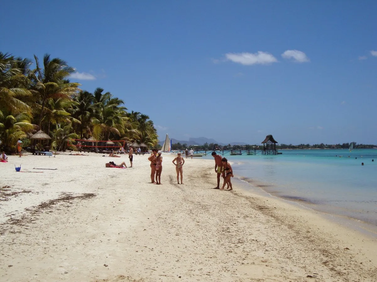 People in swimwear walking and relaxing on Trou Aux Biches beach in Mauritius with trees nearby