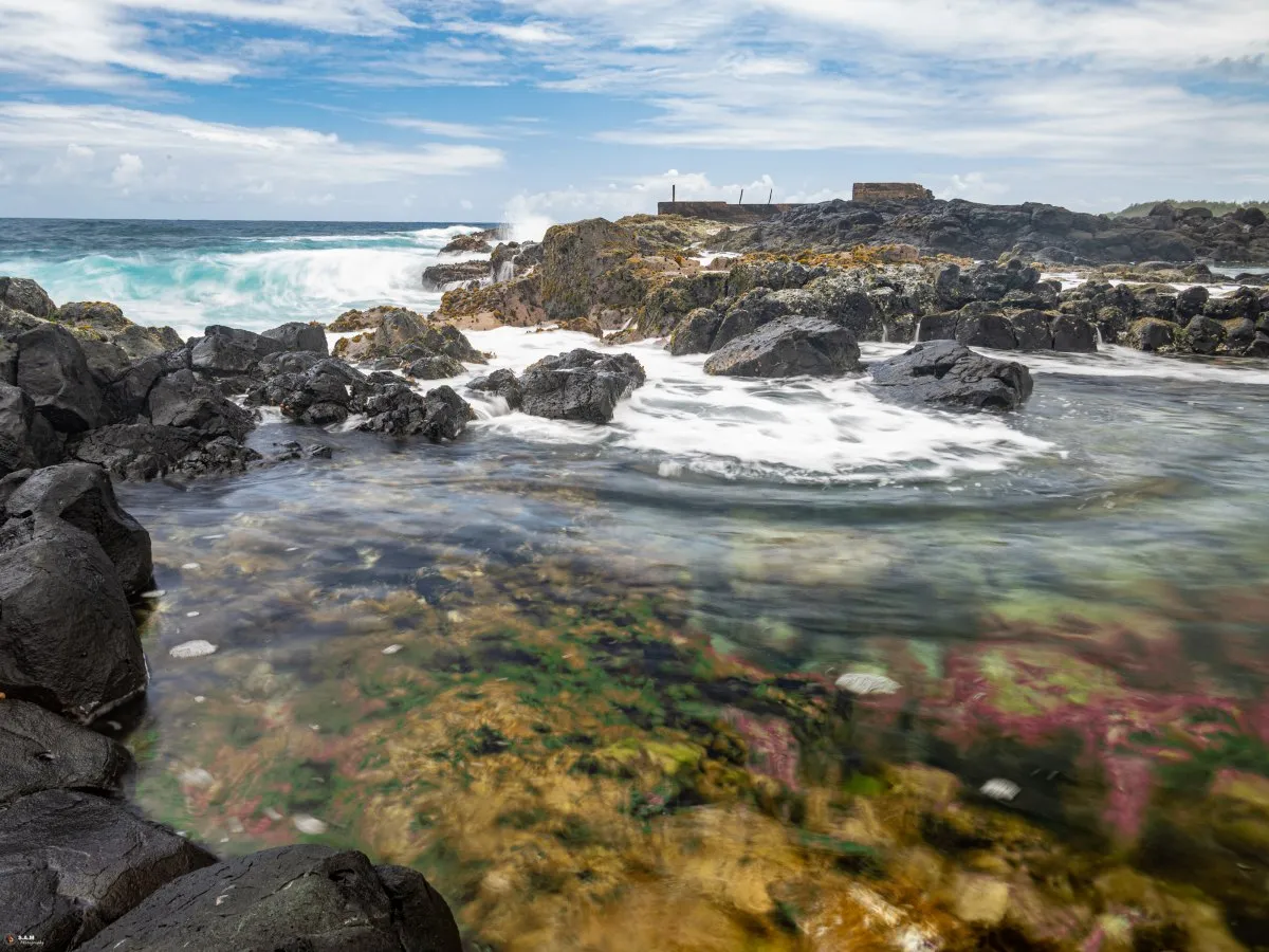 Natural rocky pool at La Cambuse beach in Mauritius with sea backdrop and warm water