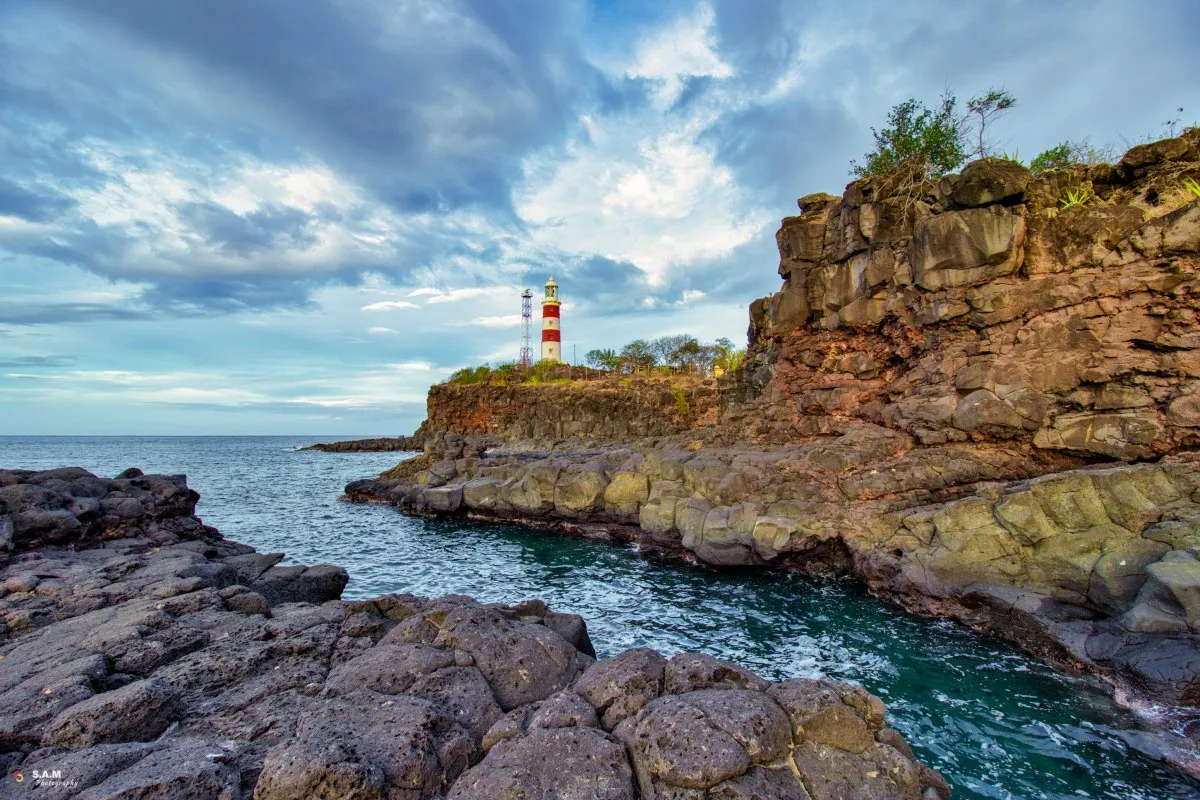 White and red striped lighthouse on volcanic Albion cliff under moody clouds in Mauritius