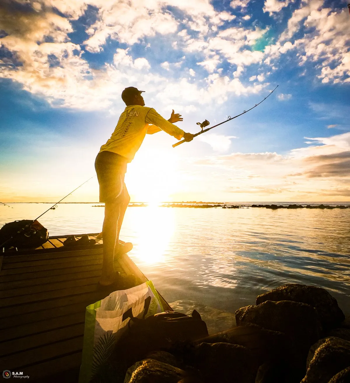 Fisherman casting rod from jetty in the lagoon at Flic en Flac, Mauritius during sunset