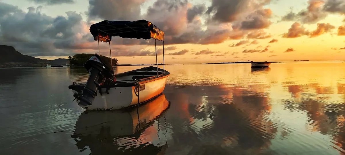 Wooden boat reflecting on calm water during sunrise at Mahebourg bay in Mauritius