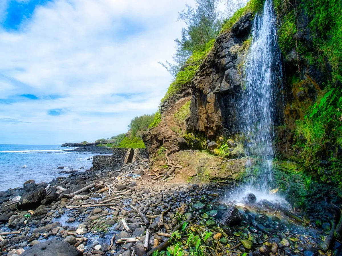 Secret waterfall flowing onto a rocky beach with lush cliffs in Mauritius