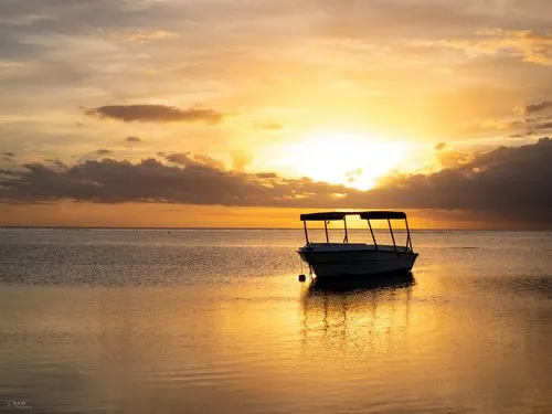 Boat silhouette with bright sunset in calm lagoon of Flic en Flac