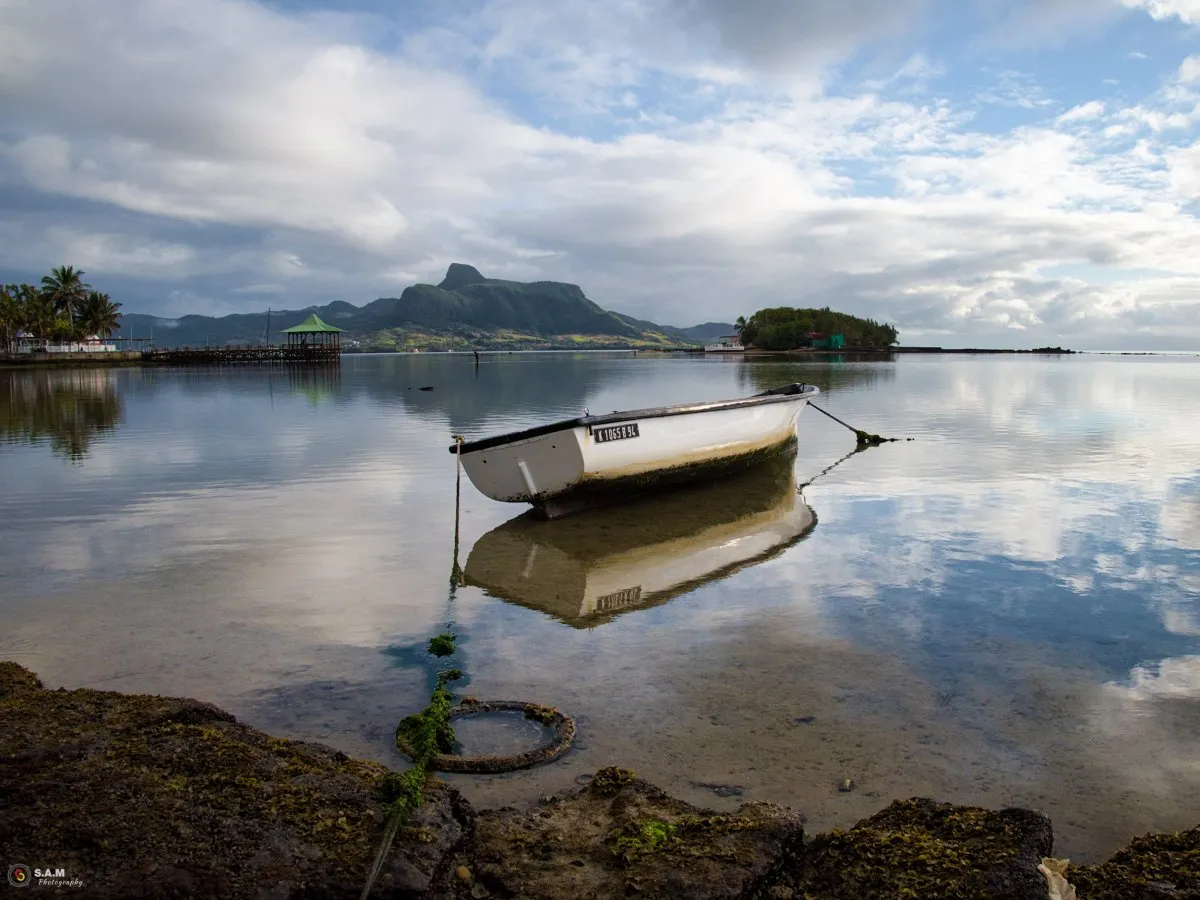 Fishing pirogue tied at low tide with reflection in lagoon water in Mahébourg, Mauritius