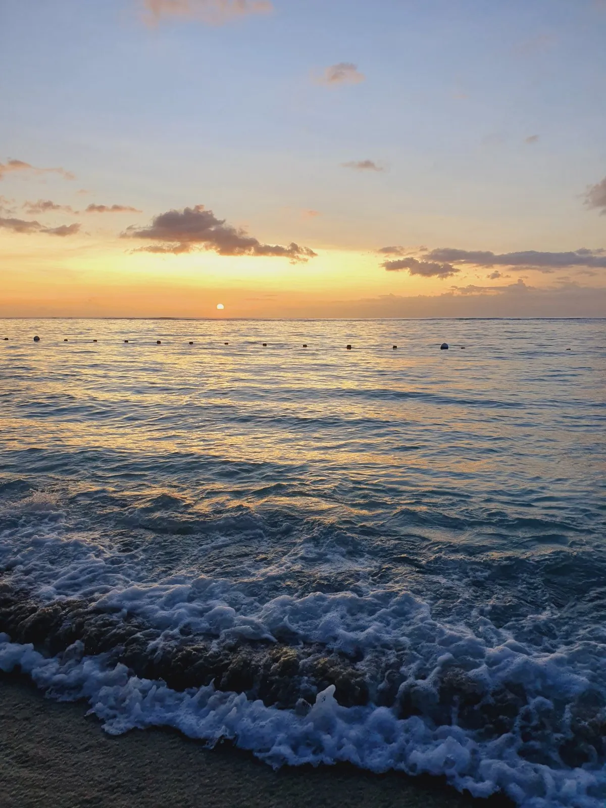Sunset waves crashing gently on Flic en Flac beach shore in Mauritius with orange sky reflections