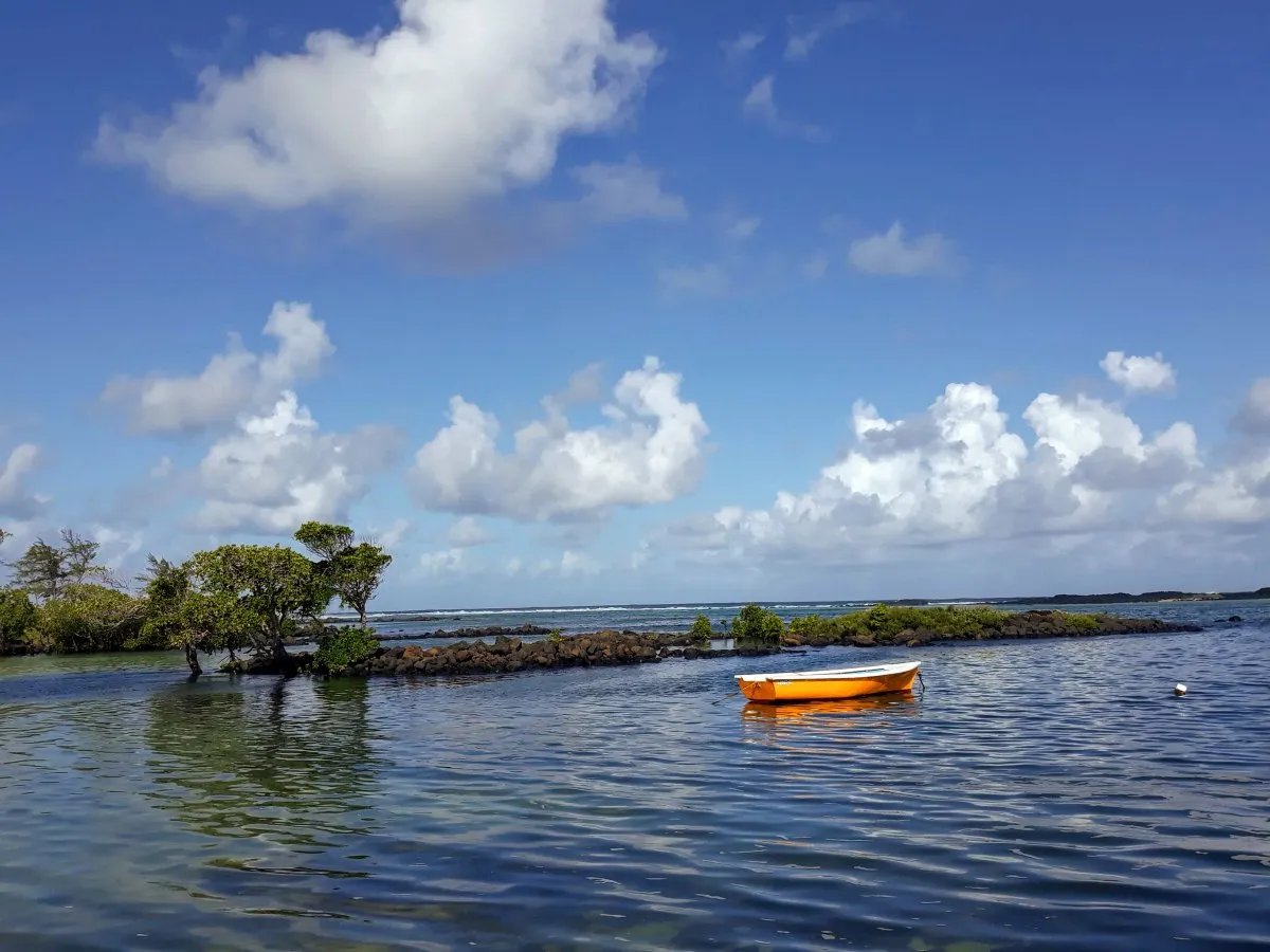 Orange pirogue on the lagoon at Le Bouchon public beach in Mauritius with plants and rocks forming an islet