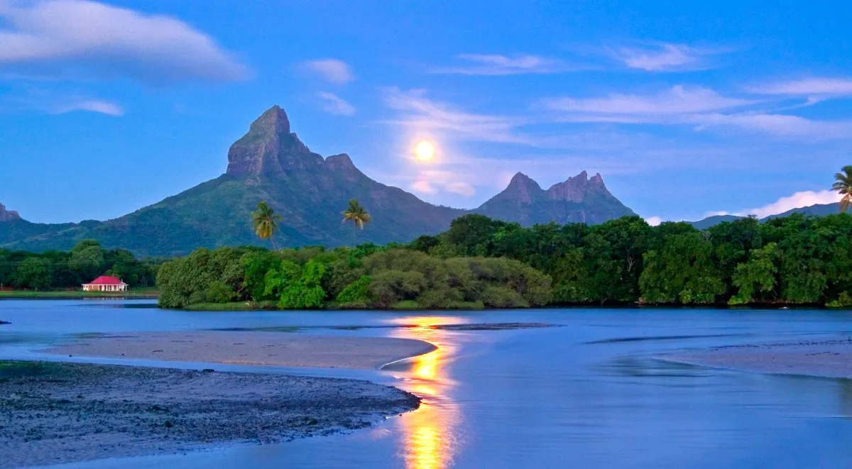 Moon rising over Rempart Mountains with reflection in Tamarin Bay lagoon at dusk in Mauritius