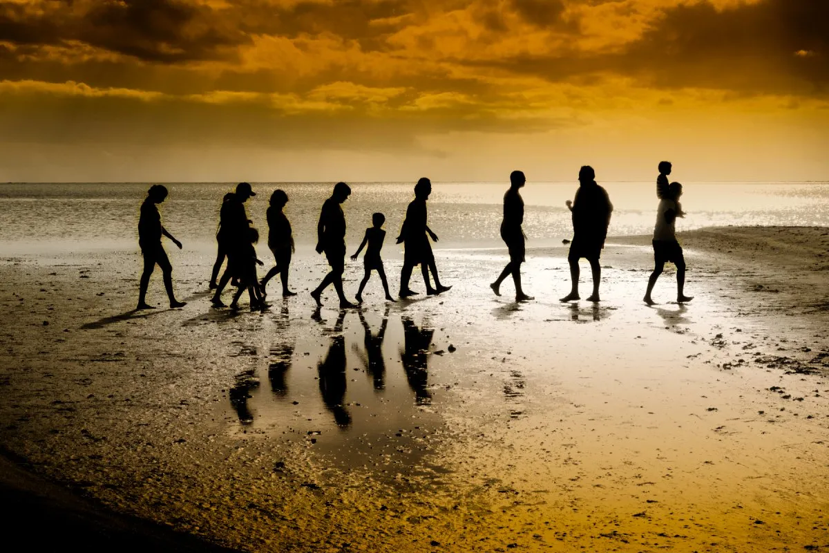 Silhouettes of people walking in single file on a Mauritian beach at sunset with golden sky reflection