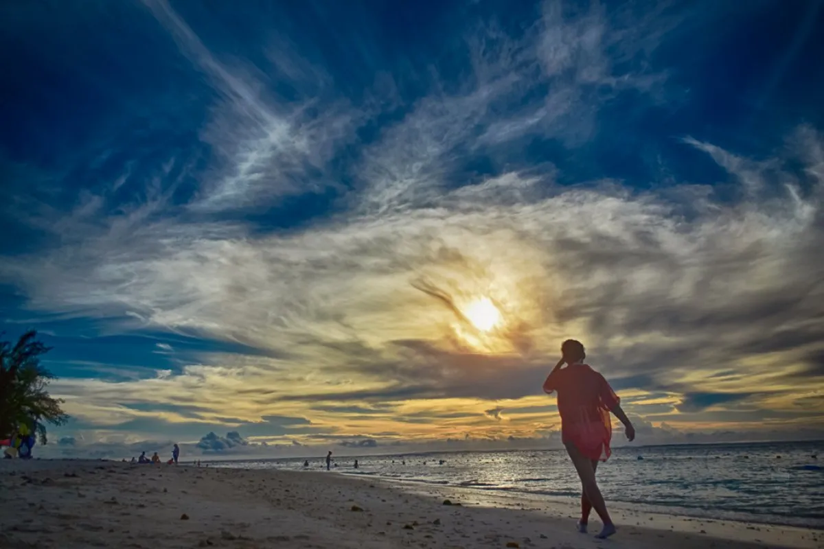 Woman in red walking on Flic en Flac beach with sunset and clouds in Mauritius