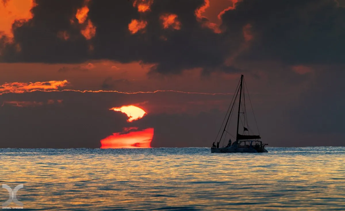 Catamaran silhouette near setting sun and clouds at Pointe d'Azur beach in Mauritius