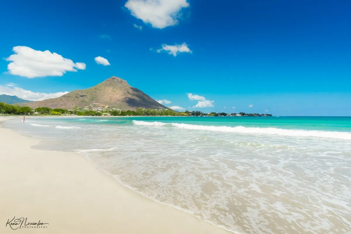 Sandy beach at Tamarin with La Tourelle mountain and a child playing in the turquoise waters of Mauritius