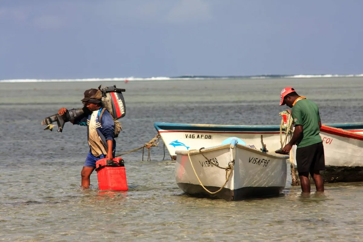 Fishermen walking in the sea carrying boat motor and gas tank at Le Morne in Mauritius