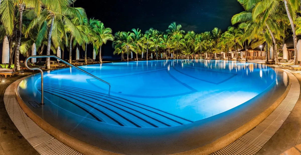 Night view of a blue infinity hotel pool surrounded by palm trees in Mauritius