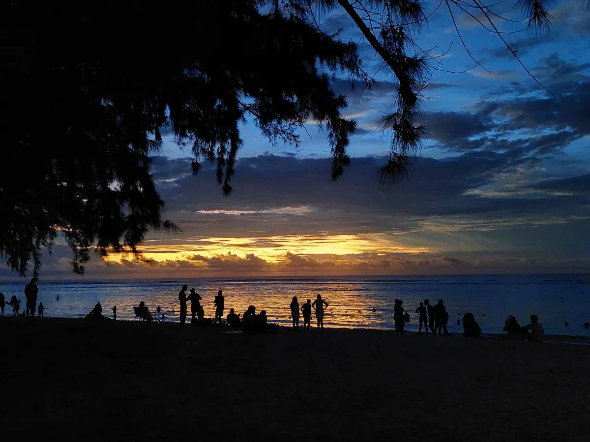 Silhouetted people standing at Flic en Flac beach after dusk with orange sky reflections in Mauritius