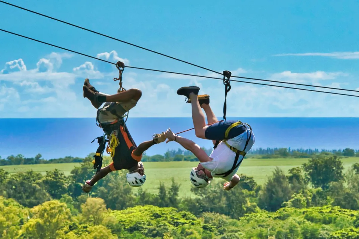Two men sliding upside down on dual zip lines at Casela Nature Park in Mauritius