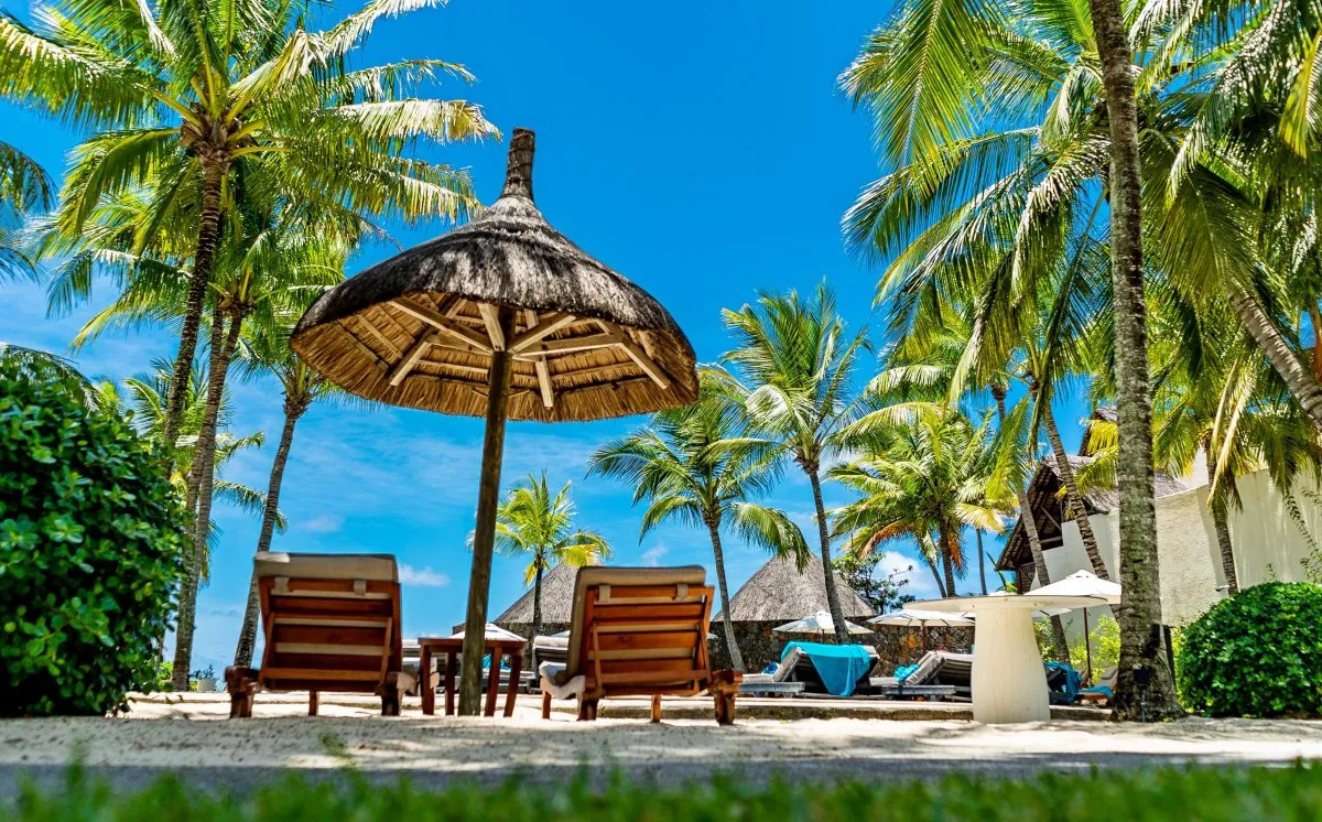 Straw umbrellas and palm trees by the pool at Constance Belle-Mare Plage hotel in Mauritius