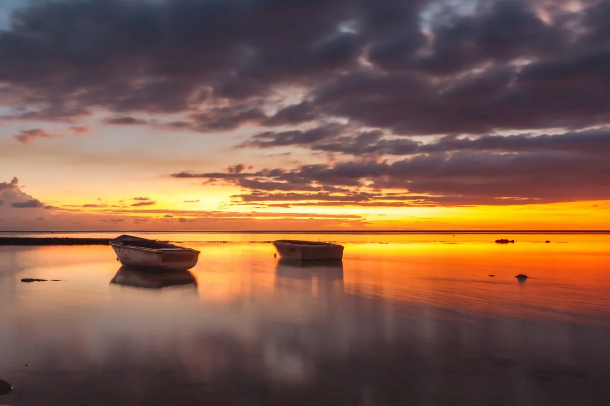 Orange sunset sky with pirogues on calm sea at Balaclava Beach in Mauritius