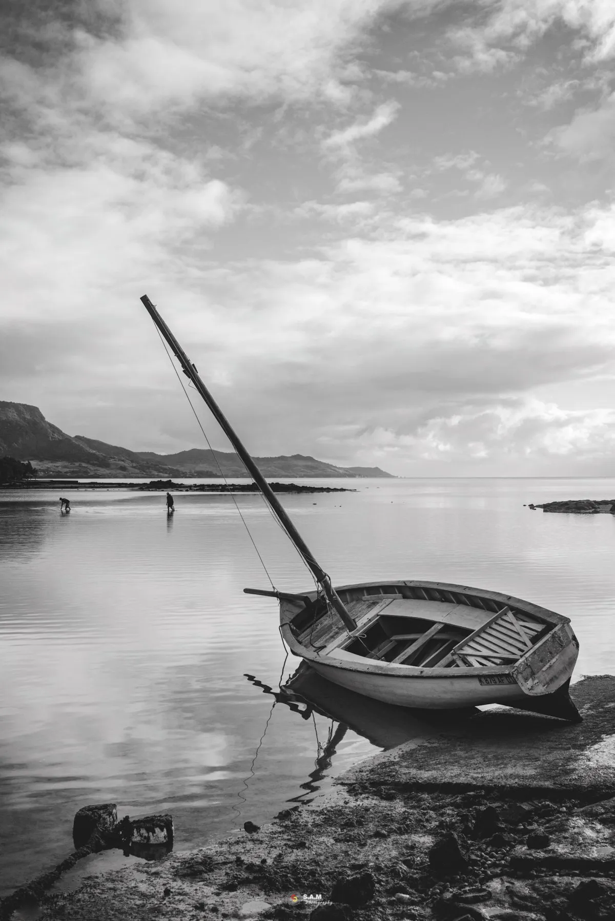Black and white photo of a pirogue and villagers in shallow water at Mahebourg Bay, Mauritius