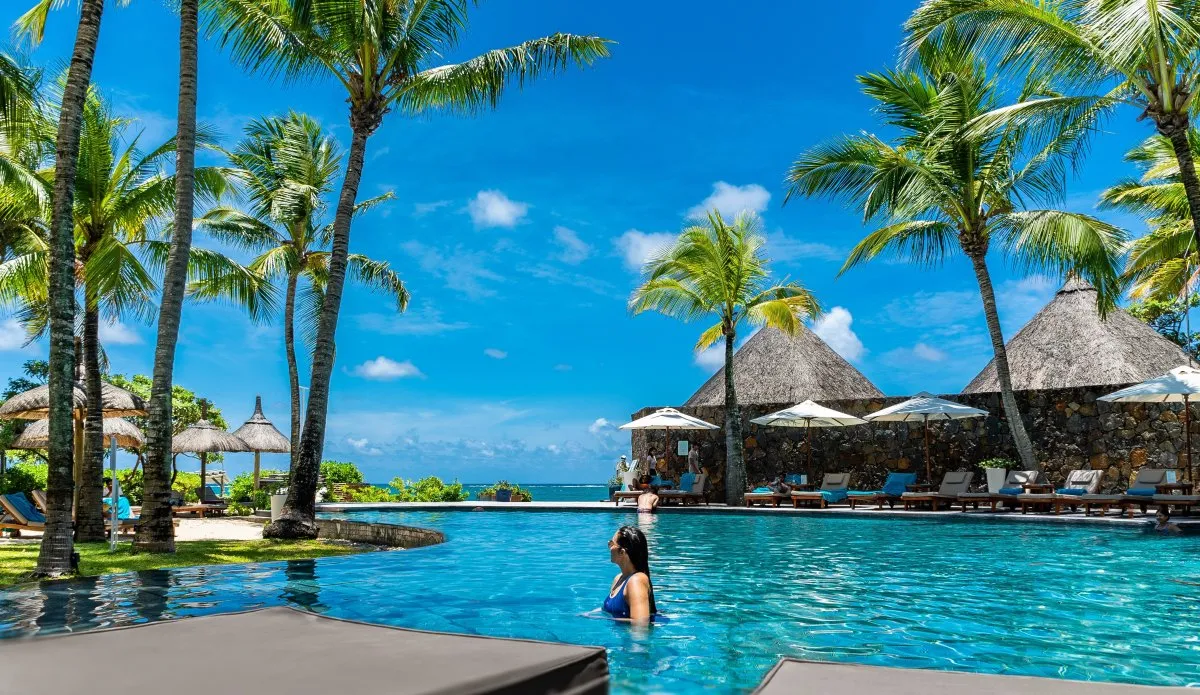 Girl relaxing in a turquoise hotel pool near the sea and palm trees in Mauritius