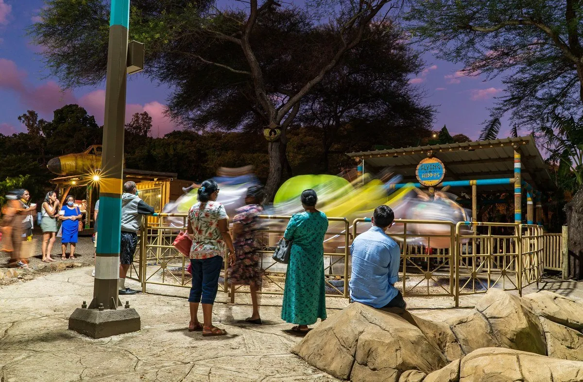 Children enjoying the Flying Hippos merry-go-round at Casela Night in Mauritius with parents watching nearby