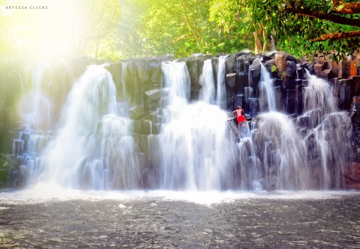 Man climbing cubic rocks at Rochester Falls waterfall in Mauritius under sunlight