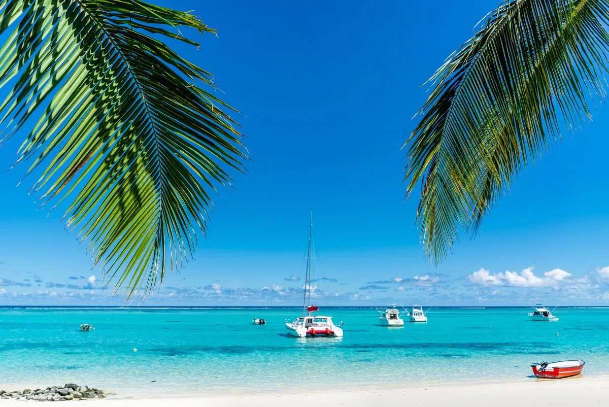 Luxury beach holiday scene at Le Paradis Beachcomber hotel in Mauritius with boats and tropical trees