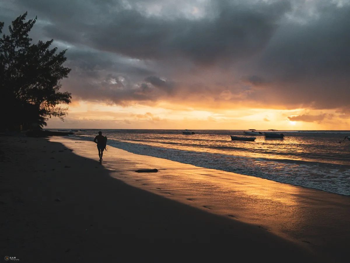 Surfer silhouette walking on Tamarin Beach at sunset in Mauritius under cloudy skies