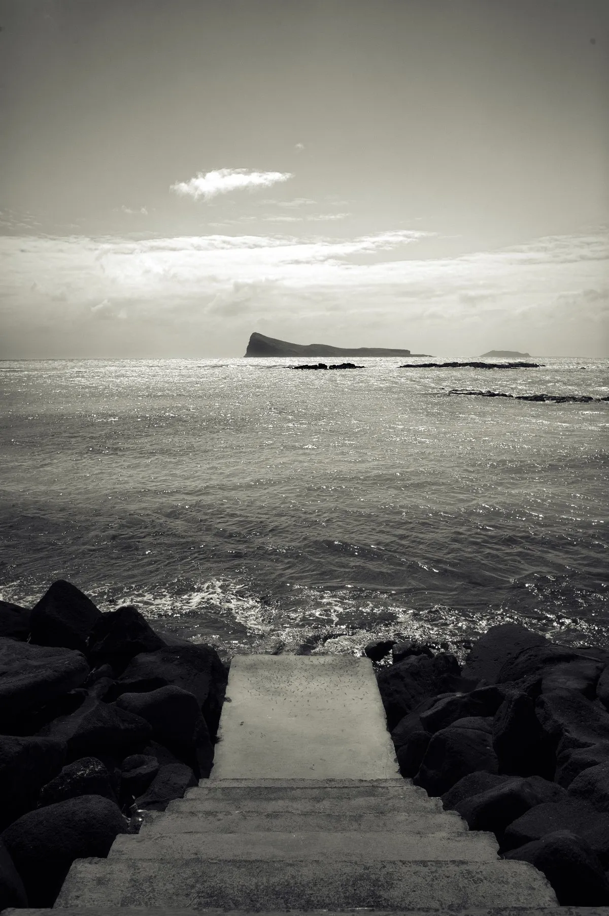 Black and white photo of a stairway leading to the sea at Cap Malheureux with Coin de Mire island in the distance in Mauritius