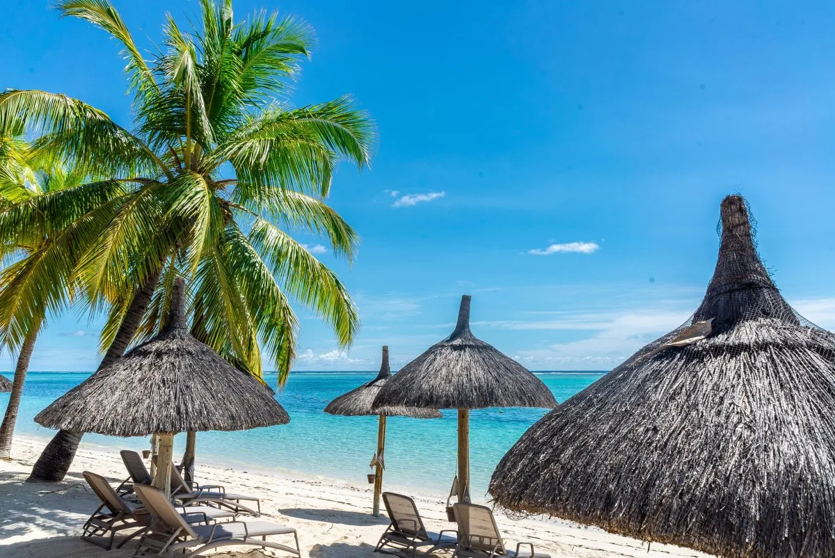 Thatched straw beach umbrellas under a bright sunny sky at Le Paradis hotel in Mauritius