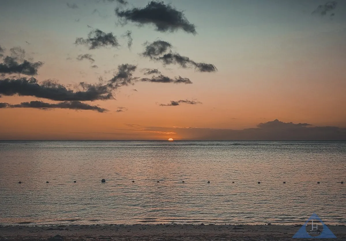 Sun setting halfway above the sea at Flic En Flac beach in Mauritius with calm skies