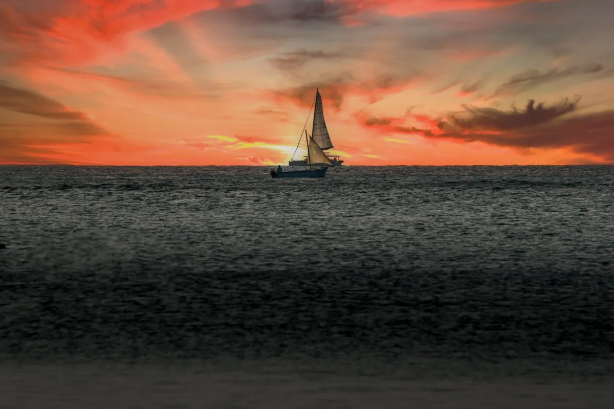 Two sailboats passing in front of a dramatic orange sunset sky at Pereybere beach in Mauritius