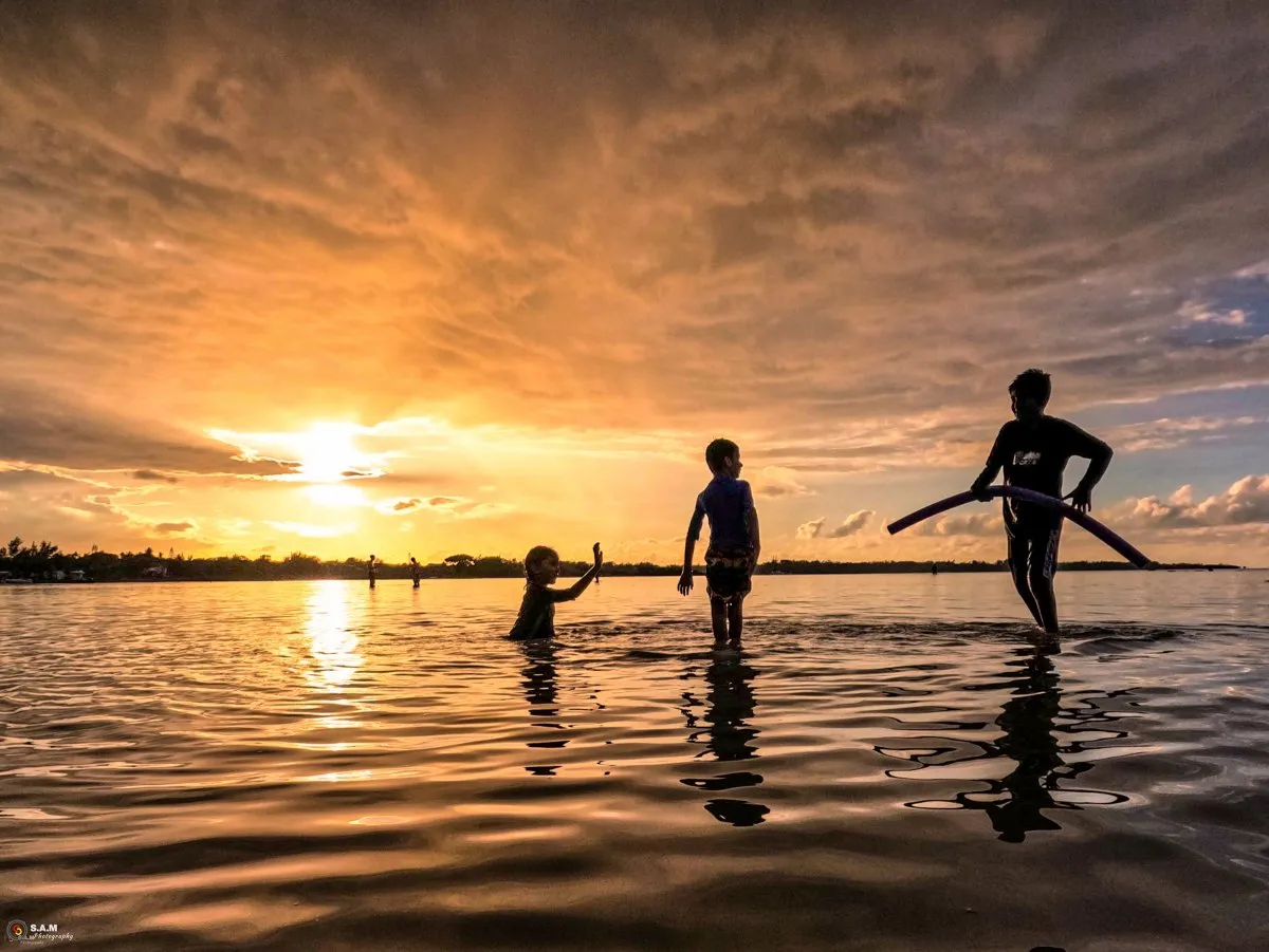 Silhouettes of children playing in the shallow sea at sunset in Mauritius.
