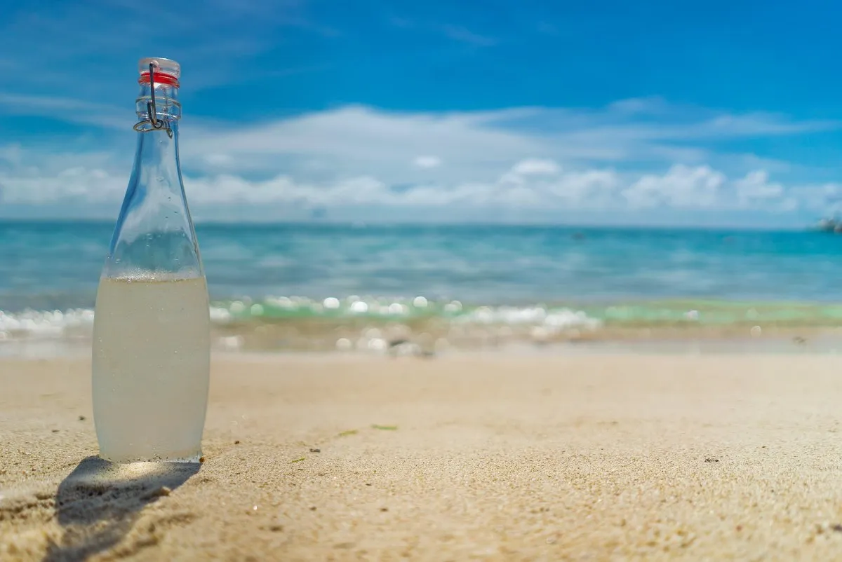 Chilled glass water bottle on Le Paradis beach with clear sea in Le Morne, Mauritius