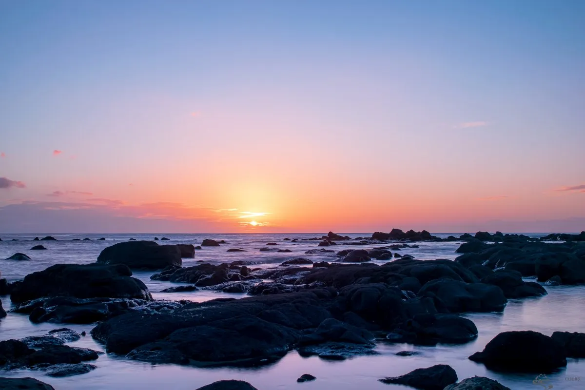 Sunset over rocky seascape at Flic en Flac beach in Mauritius with colorful sky and calm waters