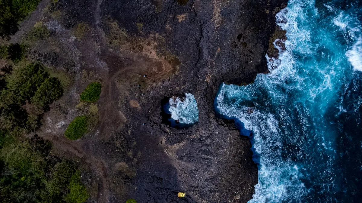 Aerial drone view of Pont Naturel in Mauritius, showing the volcanic rock arch, turquoise ocean water, dark basalt coastline and waves breaking below.