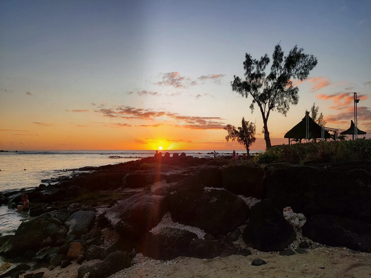 Sunset at Flic en Flac with dark volcanic rocks and a thatched kiosk near Anelia Hotel on the coast of Mauritius.