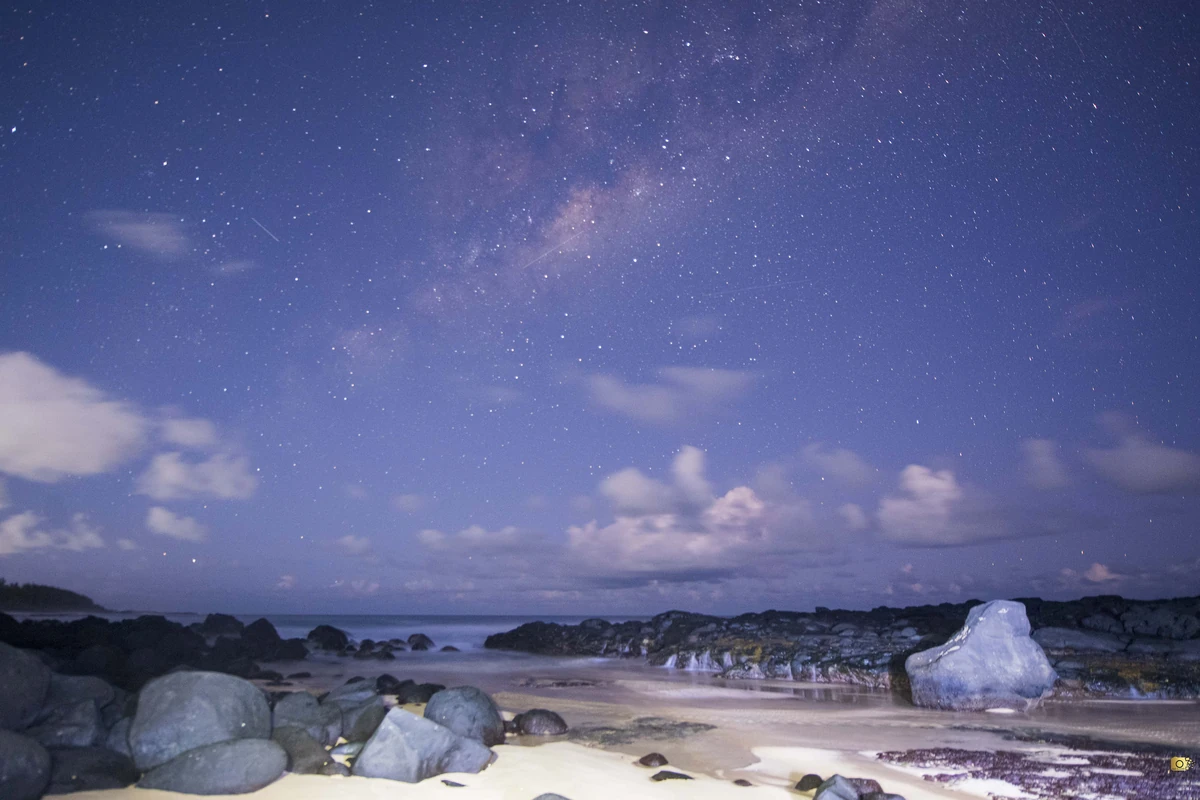 Milky Way above the rocky shore of Bénarès Beach in Mauritius at night.