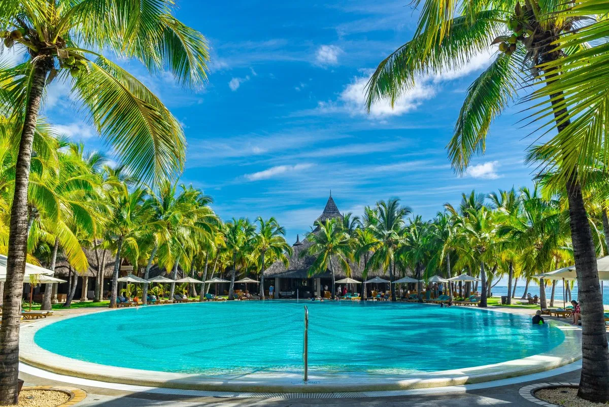 Wide turquoise swimming pool at Le Paradis Beachcomber hotel in Mauritius surrounded by palm trees and holidaymakers