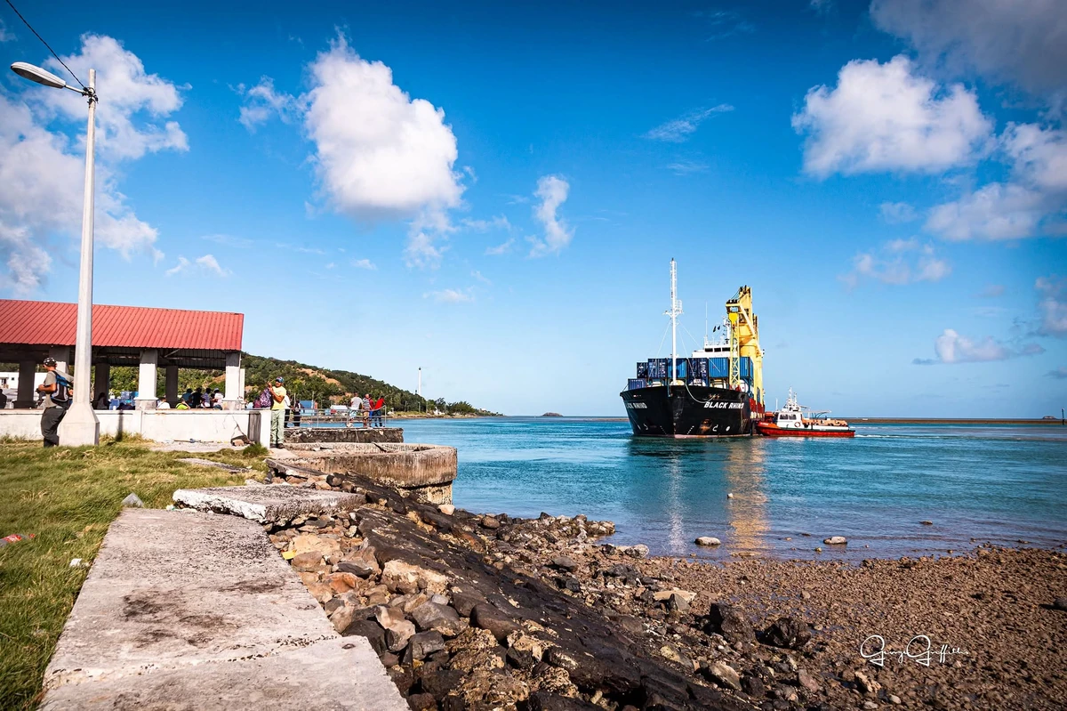 Working vessel with crane at Port Mathurin in Rodrigues Island, with a small service boat, waterfront, people, and calm turquoise water.