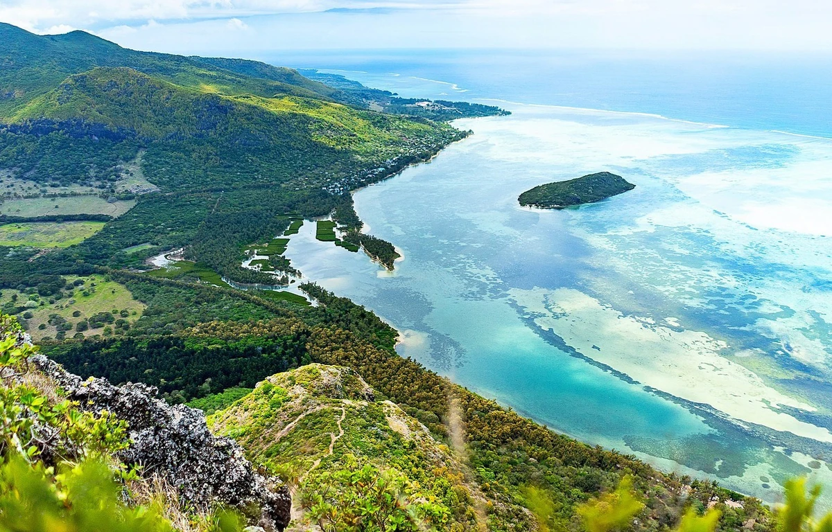 Aerial view of Îlot Fourneau from Le Morne Mountain, with the lagoon, reef patterns, and Le Morne village visible below.