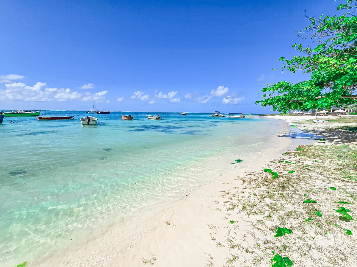 Boats floating on the turquoise lagoon of Belle Mare beach in Mauritius, with white sand, blue sky, and clear shallow water.