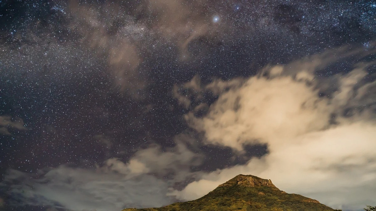 Starry night sky above La Tourelle mountain in Tamarin, with clouds and the mountain silhouette below.