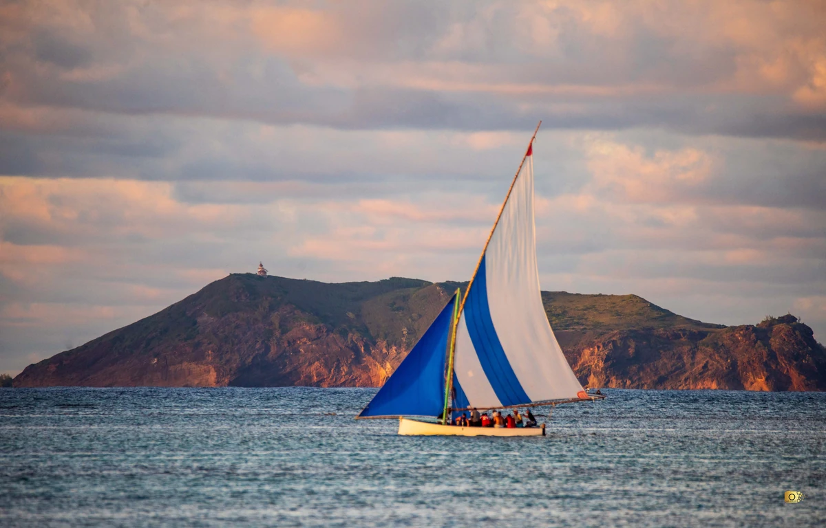 Blue-and-white sailing boat off Cap Malheureux with a rocky landform in the background.